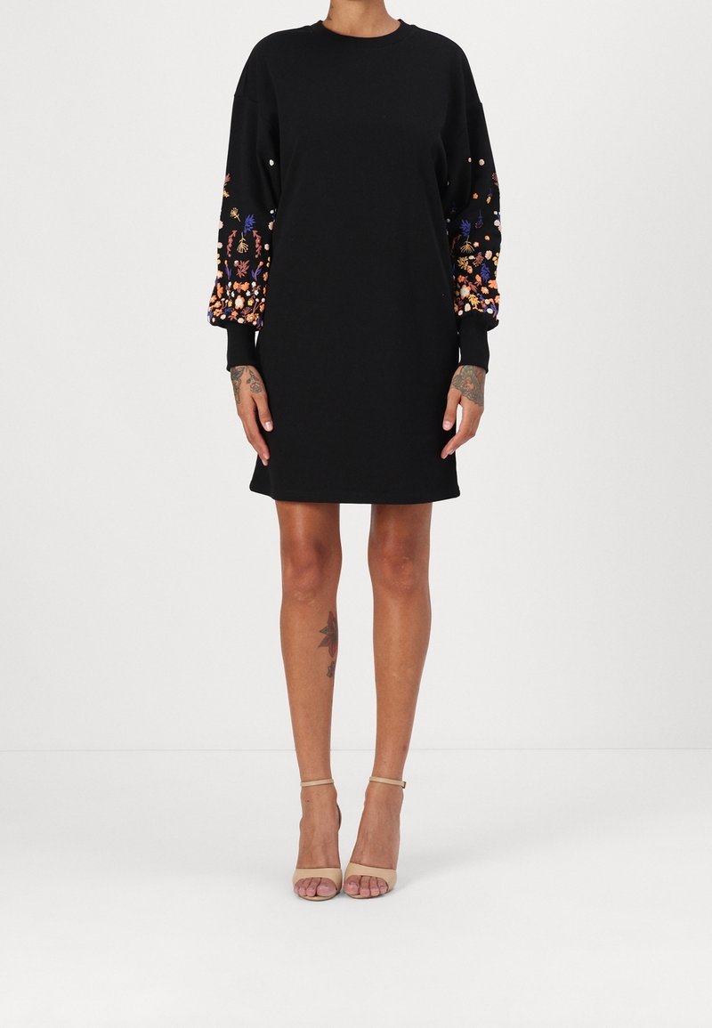 Svart klänning med rund halsringning och långa ärmar, med färgglad blomsterbroderi och rhinestones på ärmarna.
