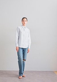 Chemise à rayures blanches et bleues avec col, associée à un jean droit délavé bleu clair et des sandales beiges.
