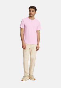 Light pink cotton t-shirt with a round neckline, short sleeves, paired with cream-colored pants and beige sneakers. Simple, casual design.