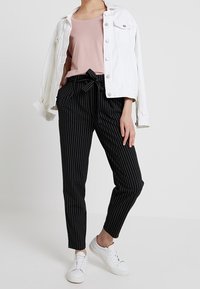 White denim jacket over a pink top, paired with black pinstriped trousers and white sneakers. Modern design with a relaxed fit.