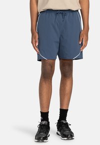 Herren Sport-Shorts in Marineblau, aus leichtem Stoff, mit elastischem Bund und Kordelzug, weißen Seiteneinsätzen und in einer Länge über dem Knie.