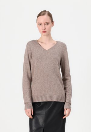 V-neck sweater in light brown, made of textured knit fabric. Features long sleeves and ribbed cuffs and hem. Worn over a black skirt.