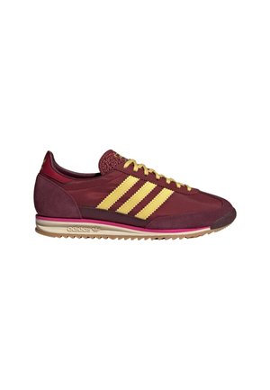 Donkerrode Adidas-sneaker met gele drie strepen, gele veters en een beige zool met een zigzagloopvlak.