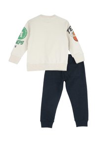 Felpa crema con accenti grafici sulle maniche, abbinata a pantaloni blu navy. Entrambi realizzati in un morbido tessuto traspirante.