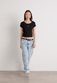 Black cropped t-shirt with a round neckline, paired with light blue distressed baggy jeans and white sneakers. Simple belt accents the waist.