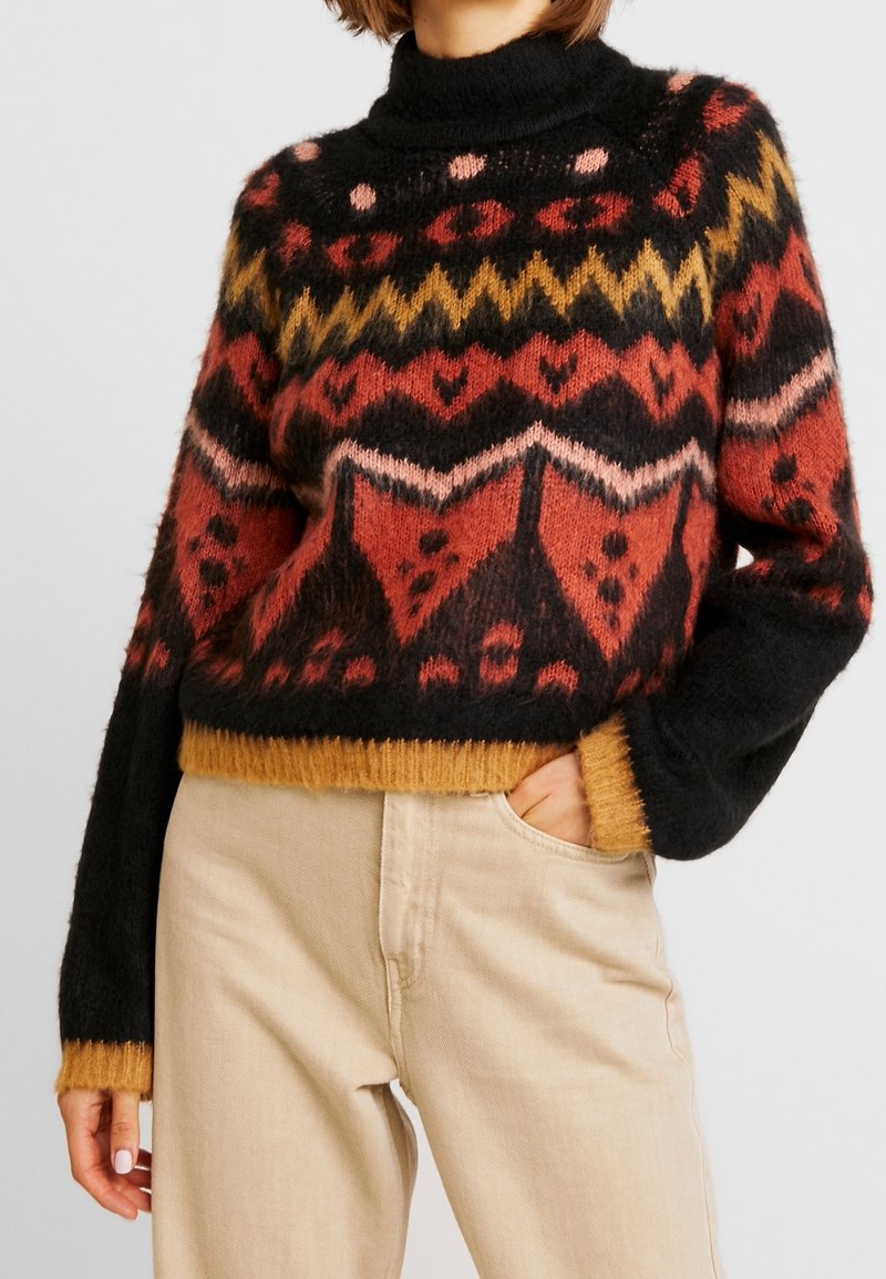 Pull en tricot avec un col montant, présentant une base noire, des motifs en rouge, or et rose, ainsi qu'un ourlet et des poignets côtelés couleur moutarde.