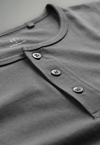 Camisa henley de algodón gris con un escote redondeado, tres botones oscuros y una textura suave. Etiqueta con "SET" visible dentro del cuello.
