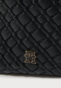 Czarna torebka z plecionej skóry z fakturowanym wzorem i złotym logo. Wyściełane sploty tworzą wyrafinowany design.