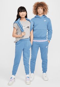 Mėlyni Nike džemperiai su atitinkamomis kelnėmis, pagaminti iš medvilnės mišinio. Mergina vilki pilką marškinėlį su juodais užrašais. Abu dėvi sportinius batelius.