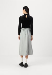 Haut en velours noir à manches longues avec des manches texturées, associé à une jupe longue gris clair à la cheville avec une taille élastique.