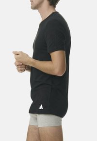 Camiseta negra de manga corta con cuello redondo, que presenta un pequeño logo blanco en el dobladillo; combinada con shorts gris claro.