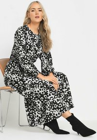 Schwarzes und weißes Leopardenmuster langärmliges Kleid mit Rundhalsausschnitt und lockerer Passform, kombiniert mit eleganten schwarzen Knöchelboots.