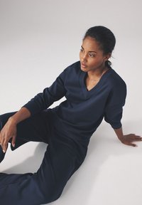 Mørkeblå loungewear sæt bestående af en V-hals sweatshirt og matchende afslappede bukser, lavet af blødt stof med ribbede manchetter og kant.