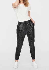 Czarne spodnie w paski zebry, wykonane z lekkiego materiału, z elastycznym pasem i bocznymi kieszeniami, zestawione z białą koszulką i trampkami.