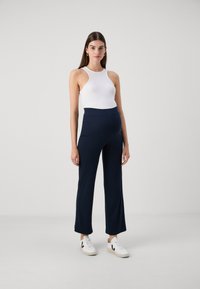 Navy blue, high-waisted trousers in a smooth, stretchy fabric. Pairing with a white sleeveless top and white sneakers, featuring black accents.