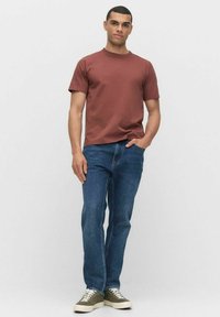 Brun crew-neck t-shirt, blå straight-leg jeans og grønne low-top sneakers. Glat stof, afslappet pasform, minimalistisk design.