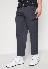 Dark gray cargo pants with elastic waistband and side pockets, paired with white Nike sneakers featuring black accents.