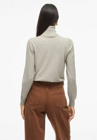Svijetlosiva turtleneck pulover sa dugim rukavima, uparena sa smeškastim hlačama s visokim strukom koje imaju strašnje džepove i glatku teksturu.