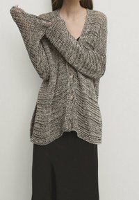 Neulottu cardigan neutraaleissa sävyissä, joissa on teksturoitu kuvio, V-pääntie, pitkät hihat ja kaksi nappia edessä.