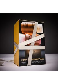 Zestaw prezentowy OUAI w złoto-czarnym pudełku, zawierający trzy pojemniki w kolorze brązu i bieli, owinięte lekką kokardą. Widoczne etykiety.