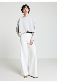 Felpa oversize grigio chiaro con spalle scese, abbinata a pantaloni bianchi a gamba larga e vita alta e scarpe con tacco decorate.