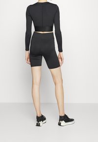 Top corto negro de manga larga con cintura ajustada, combinado con pantalones cortos a la mitad del muslo a juego. Footwear presenta un diseño negro con suela blanca.