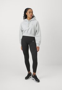 Felpa cropped grigia con cordoncino e leggings neri con un motivo sottile, abbinati a scarpe da ginnastica nere.