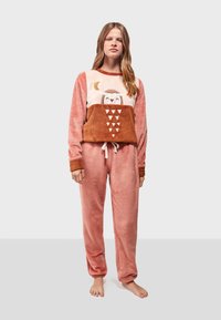 Fleece-Loungewear-Set mit einem rosa und braunen Eulenmotiv auf der Oberseite, kombiniert mit sanften rosa Hosen, beide mit gerippten Akzenten und Kordelzug.