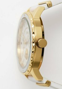 Gouden horloge met een ronde wijzerplaat, witte lederen band, getextureerde bezel en gouden accenten. Beschikt over een witte dial met gouden markeringen en wijzers.
