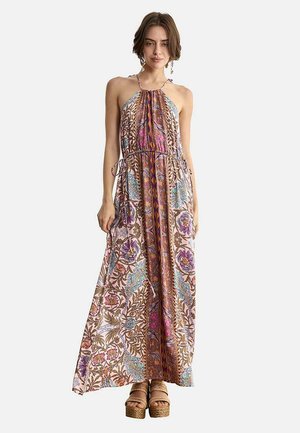 Mujer vistiendo un vestido largo sin mangas con estampado floral, cuello halter y lazos en la cintura, combinado con sandalias de plataforma.