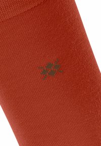Calza rossa lavorata a maglia con una consistenza liscia e un sottile design di teschio e ossa incrociate marroni sul lato.