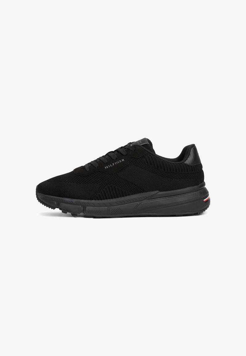 Chaussure de running en maille noire avec un design à lacets, de marque "Hilfiger", et une semelle texturée avec une petite bande rouge, blanche et bleue au talon.