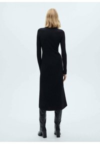 Robes en tricot côtelé noir à manches longues, silhouette ajustée et longueur mi-mollet, associées à des bottes noires montantes.