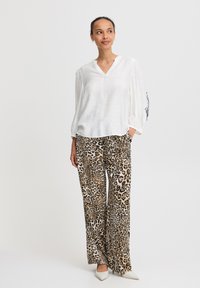 Hvid, letvægts skjorte med lange ærmer og V-udskæring; parret med løstsiddende bukser med leopardprint i beige og sort; båret med hvide hæle.