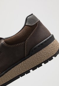 Braunes Lederschuh mit einer strukturierten beigen Sohle, der dunkle Akzente, kontrastierende Nähte und ein tief ausgeschnittenes Design aufweist.