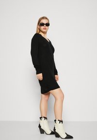 Vestuário preto de mangas longas com um design de decote em V, feito de um material leve. Combinado com botas de tornozelo em estilo cowboy, pretas e brancas.