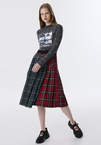 Graues Langarmshirt mit Paillettenverzierungen und Filmgrafik. Bunt karierten Midirock mit Falten. Schwarze Sneaker runden das Outfit ab.