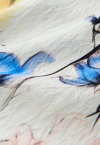 Tissu blanc à surface texturée présentant des motifs floraux délicats en bleu et rose reliés par de fines tiges noires.