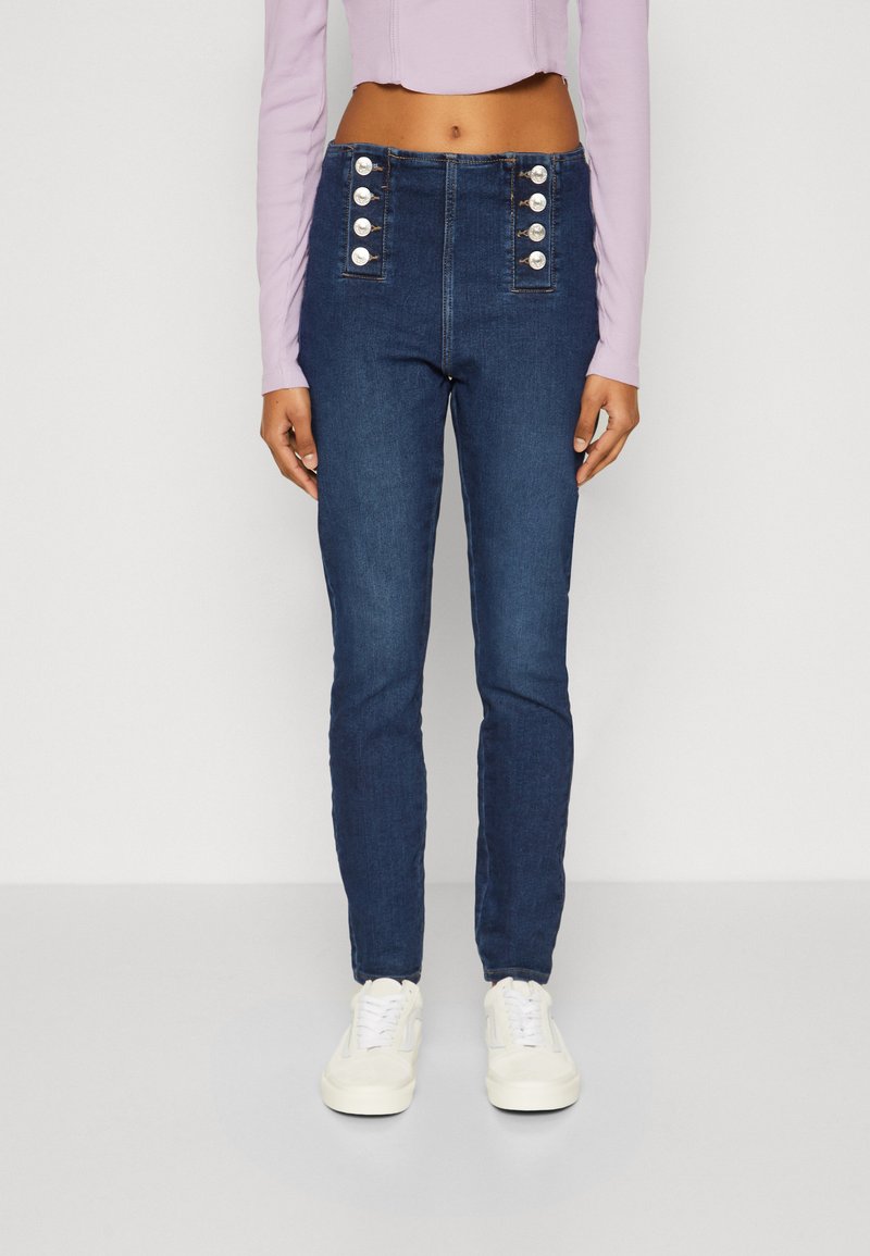 Jeans de mezclilla de tiro alto en azul oscuro con cinco acentos de botones plateados en los bolsillos frontales, diseño ajustado y textura suave.