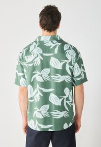Kortermet skjorte med knappestolpe i grønn med hvit blomsterprint; avslappet passform, krage og lett stoff.