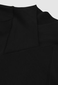 Czarny top z wysokim kołnierzem i unikalnymi detalami szwów. Miękka tekstura z gładkim wykończeniem. Charakteryzuje się minimalistycznym designem i nowoczesnym krojem.