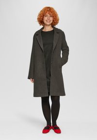 Grauer Wollmantel mit Reverskragen, langenärmeln und geradem Schnitt. Über einem dunklen, strukturierten Kleid getragen, kombiniert mit roten Ballerinas.