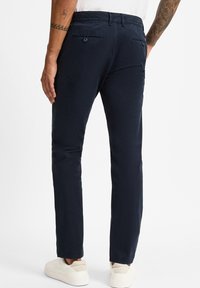 Chinos blu navy realizzati in tessuto liscio con una vestibilità slim. Presentano due tasche posteriori e chiusura con bottone. Indossati con sneaker chiare.