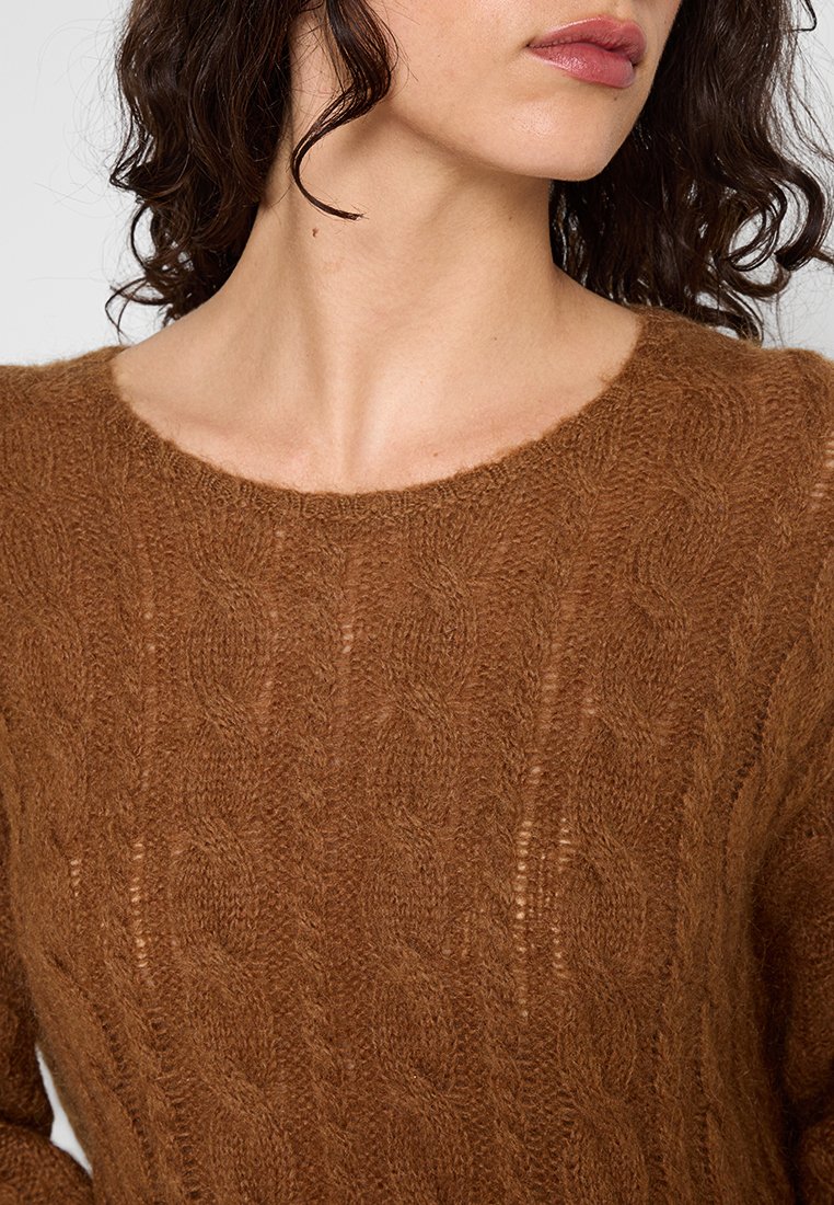 Brązowy sweter w splot cable, wykonany z miękkiej, teksturowanej przędzy. Posiada szeroką, okrągłą dekolt oraz skomplikowane detale wzoru.