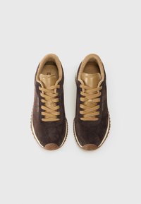 Pruun nahast sportjalatsid beežide nahkaaktsentidega, ümar varvas ning tekstuuriga kummist tallad. Omab sobivaid paelu ja pehmendatud krae.