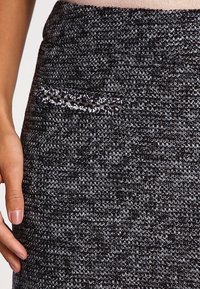 Svart, texturerad kjol med ett vävt mönster och ett litet dekorativt ficka. Slät yta med en figursydd design.