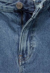 Jeans de mezclilla azul claro que presentan un botón y cremallera de metal, costuras visibles y una textura suave a lo largo de la cinturilla y el frente.