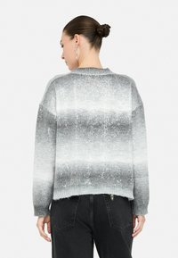 Pulover cu un gradient gri și alb, cu o strălucire subtilă, guler rotund, mâneci lungi și un tiv scurt, asortat cu pantaloni negri cu talie înaltă.