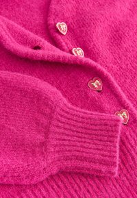 Fluffy lyserød cardigan med hjerteformede guldknapper og ribbede manchetter. Blød tekstur med et hyggeligt design og en lys farve.