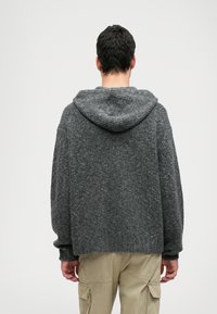 Sivý pletený hoodie s rebrovanou textúrou a uvoľneným strihom. Obsahuje veľkú kapucňu a spadnuté ramená, kombinovaný s béžovými cargo nohavicami.